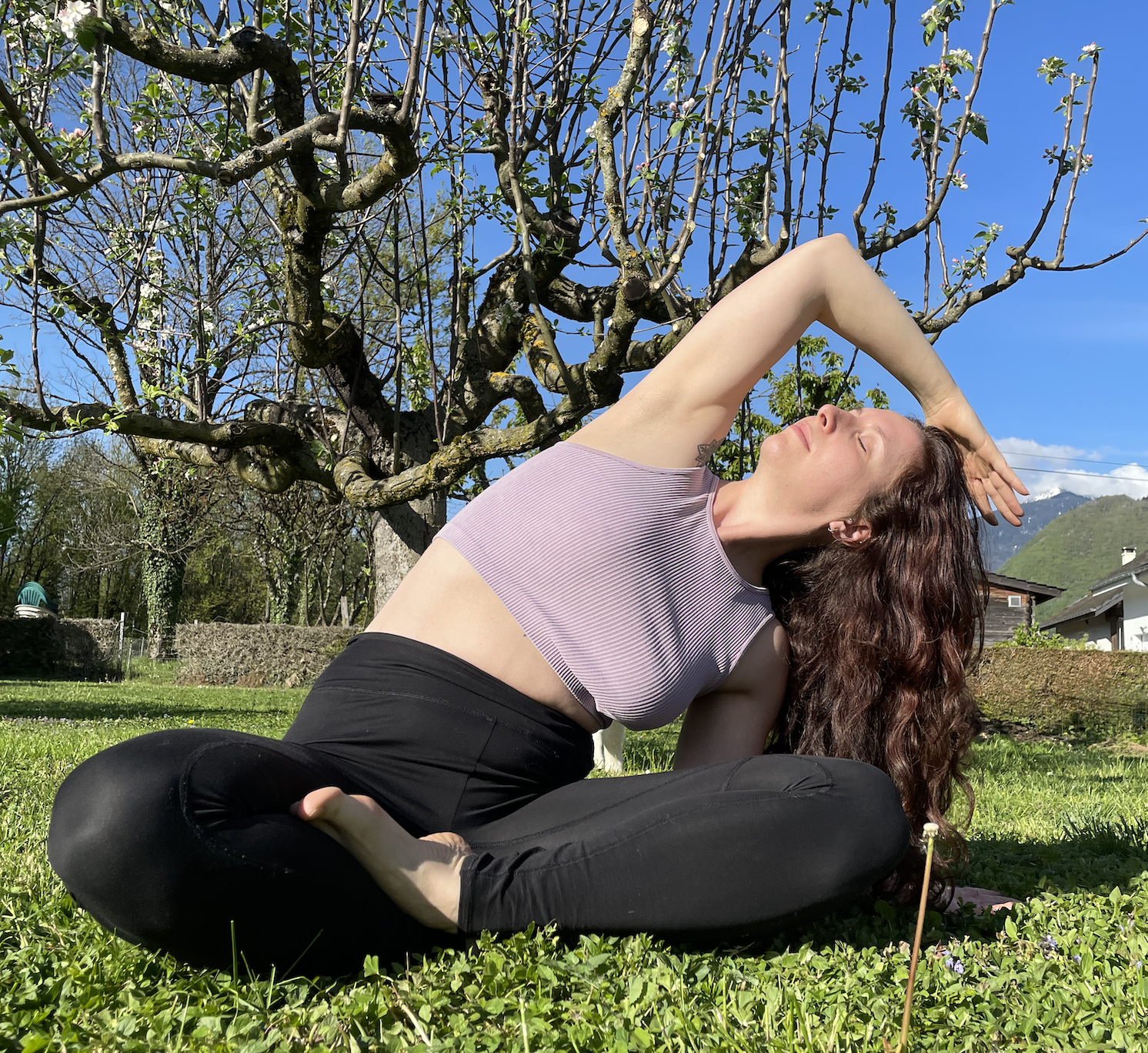 Femme pratiquant du yoga : assise dans l'herbe au soleil en tailleur, étirement latéral